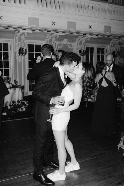 A black and white image of a man and woman kissing on the dance floor at a wedding. 