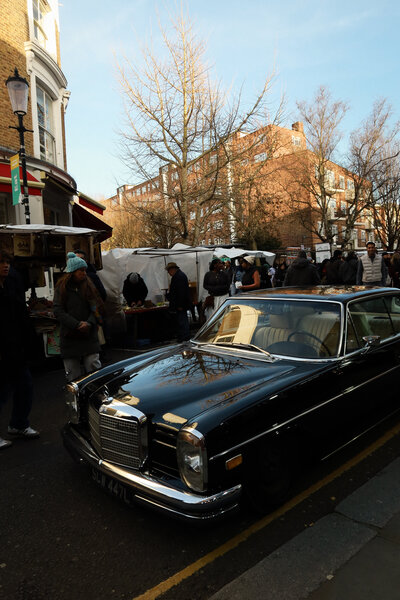 Old car parked on a street with people walking around it