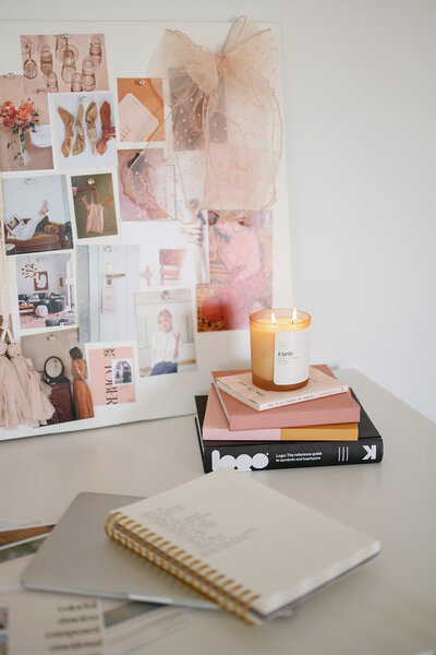 A candle on top of a stack of books in front of a collage board of photos