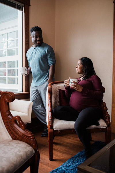 Couple relaxing in their home near a large window, enjoying their morning coffee while taking maternity photos in Tacoma