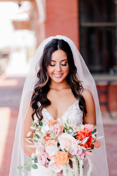Bride smiling while holding a colorful bouquet and wearing a veil outdoors