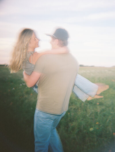 Hazy film photo of man carrying woman in a grassy field