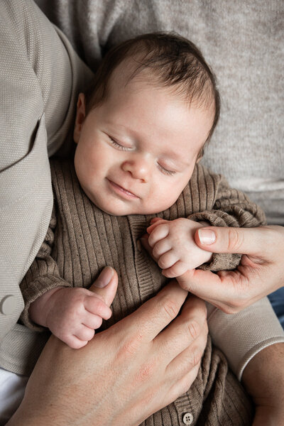Baby slaapt bij ouders in hun handen tijdens een ontspannen newbornshoot.