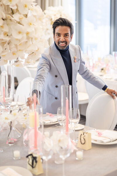 Well tailored man, Shaun, in a gray blazer with a pink boutineer smiling and setting a beautiful wedding tablescape