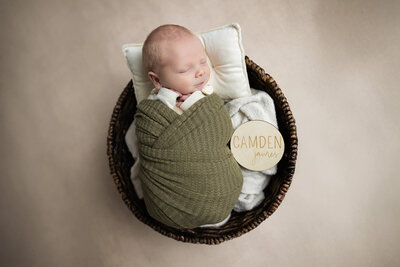 Newborn boy swaddled in bowl using green wrap and smiling, photographed in La Vernia