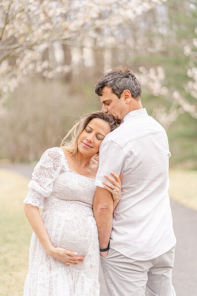 dad kissing expecting mom's temple during their maternity photos in Vienna, VA, taken by a Fairfax, Virginia maternity photographer