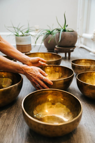 Boston Branding Session image for an acupuncturist; 7 brass Tibetan bowls lined up in front of a window with green plants behind. Her hands reach down to hold the middle bowl.