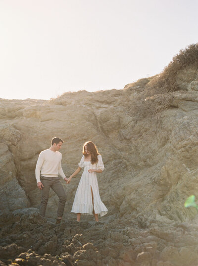 Engaged couple walking through rocky beach in Malibu