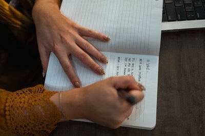 Woman writing vows in journal with a pen on a desk