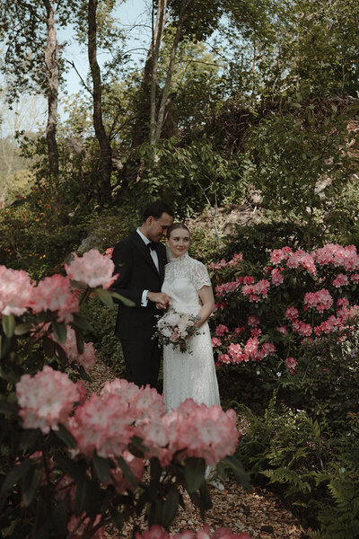 Brudpar står i en rosa blommig trädgård