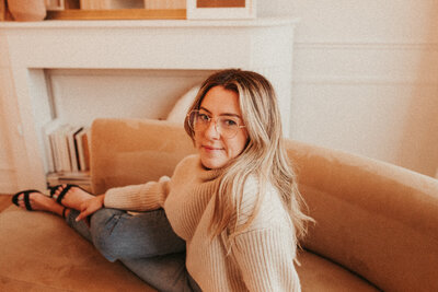Girl is sitting on couch and smiling while wearing a turtleneck