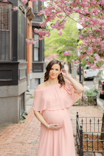 pregnant woman holds baby bump and smiles at camera during boston maternity photoshoot