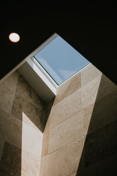 The luxurious skylight in this expertly tiled wall unveils a clear blue sky, with sunlight artfully casting shadows—an exquisite touch by a renowned Newcastle interior designer, highlighting the pinnacle of luxury home design.