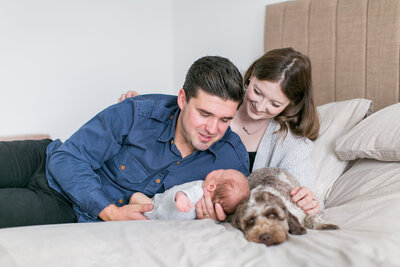 Family photography of a other and Father cuddling their newborn baby on their bed with their dog in Surrey