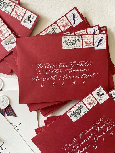 Red Christmas card envelopes with white ink calligraphy and vintage postage stamps.