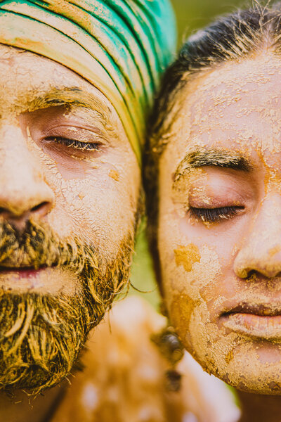 A bride and groom with haldi turmeric on their faces pose for a closeup picture