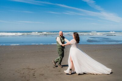 a couple in wedding attire spinning on a beach in Washington.