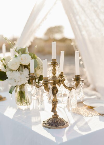 Outdoor coastal wedding setup featuring floral bouquets and a candelabra on a decorated table.