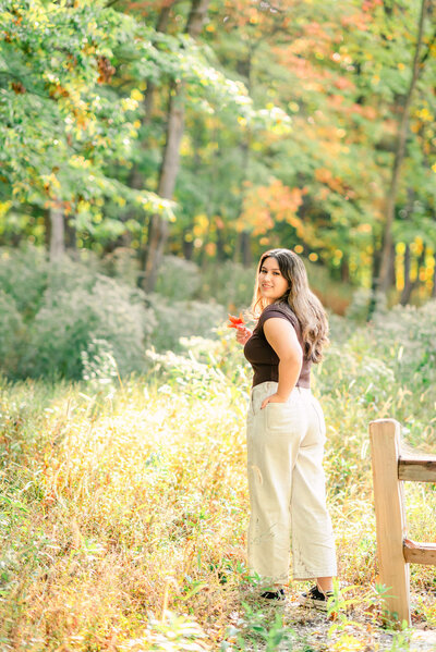 High school senior girl in the fall woods, holding a red maple leaf by Chicago senior photographer Kristen Hazelton