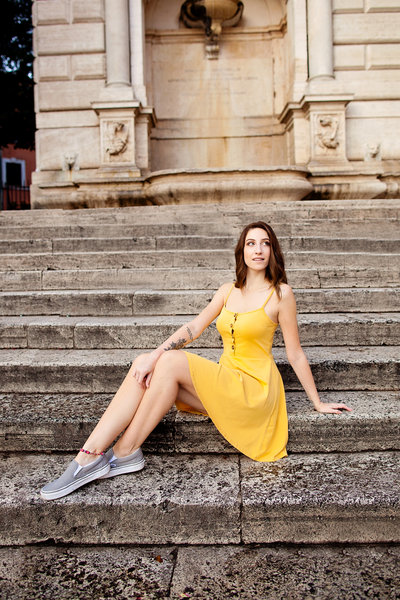 A girl solo traveler in a yellow dress sitting on the steps in Piazza Trilussa. Taken by Rome Vacation Photographer, Tricia Anne Photography