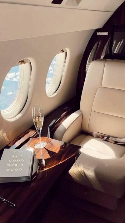 Passenger savoring first-class comfort and champagne while gazing out at clouds from the window.
