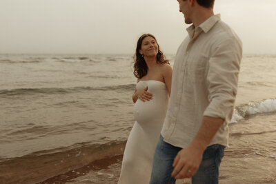 couple walking on beach for maternity photos in pei