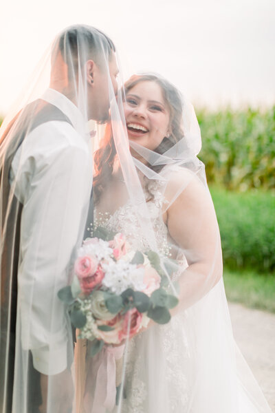 Bride and groom under a veil, sunset light coming through the fabric, bride laughing past the camera