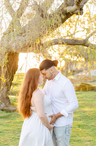 husband holds wife's pregnant stomach with light in the background