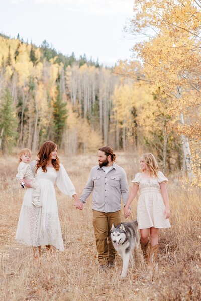 A family of 4 walk together in a mountain trail holding hands with Husky walking with them 
