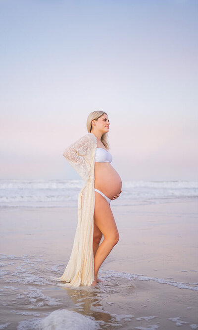 pregnant mum to be with her family on the beach with pink sunset backdrop in Brisbane