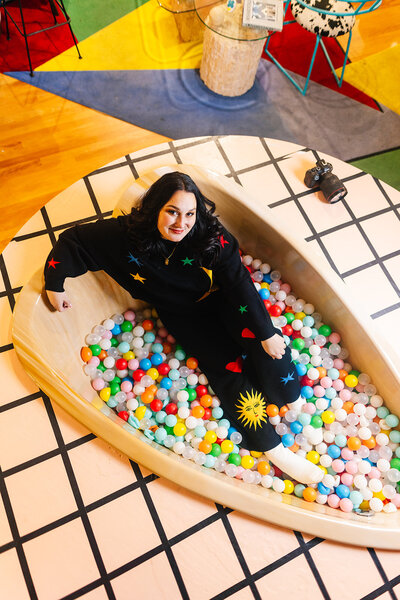 photographer sitting in ball pit at cool funhouse for brand photos