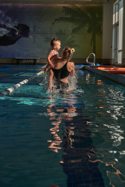 Swim coach guiding a toddler in learning how to swim