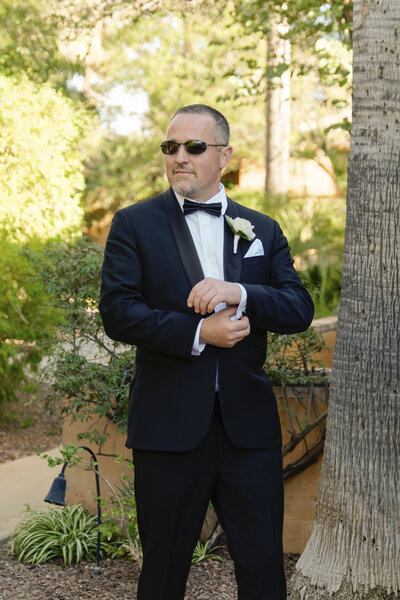 Groom adjusts his cufflinks while wearing his wedding tuxedo