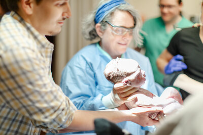 doctor is guiding newborn into fathers hands during birth