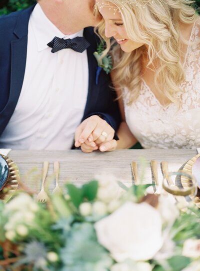 Bride and groom sat at a table holding hands at Long  Island wedding