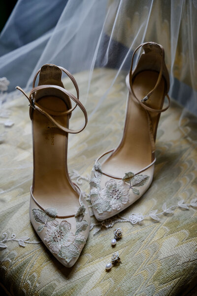 Floral embroidered heels sit beside a wedding invitation and earrings on a green fabric