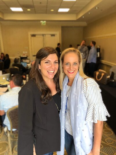 Amy Porterfield and Salome Schillack standing together and smiling in a conference room