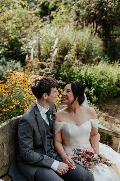 Bride and groom sat on a bench in front of a garden filled with yellow flowers at Miskin Manor