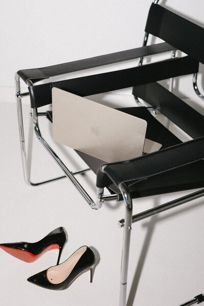Modern silver and black chair styled with a MacBook and Christian Louboutin shoes, capturing a sleek and luxurious branding aesthetic.