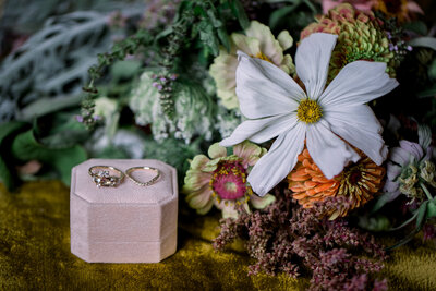 Wedding rings on top of a pink velvet ring box next to a bouquet of locally grown flowers 