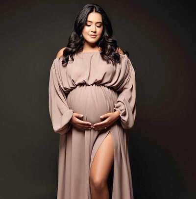 PREGNANT MOM POSED FOR A MATERNITY SESSION WEARING A CHAMPAGNE COLORED LONG-SLEEVED DRESS AND POSED FACING FORWARD.