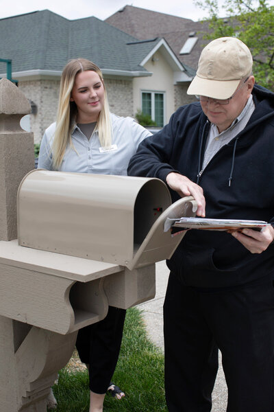 Elderly man smiling while walking to the mailbox with caregiver beside him