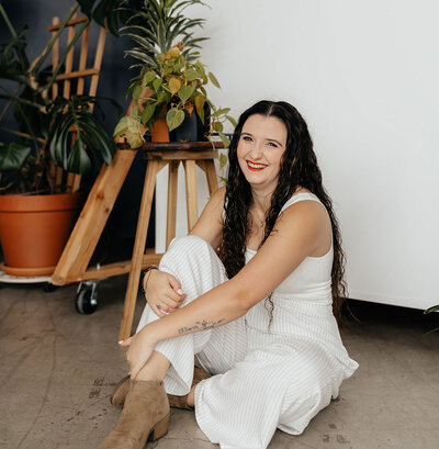 Taysha smiling at the camera sitting on the ground with plants around her.