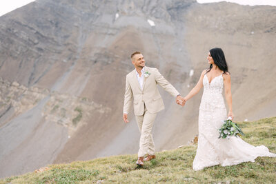 Bride and groom walk hand in hand along a mountain ridge, celebrating their elopement with breathtaking views