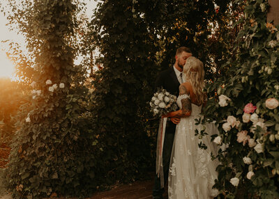 Bride and groom kissing next to rose bush