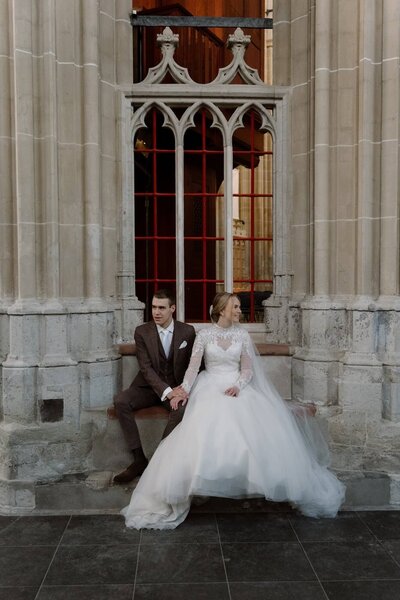 Bruid en bruidegom op een bankje voor een kerk, vastgelegd door trouwfotograaf Julia de Groot uit Utrecht