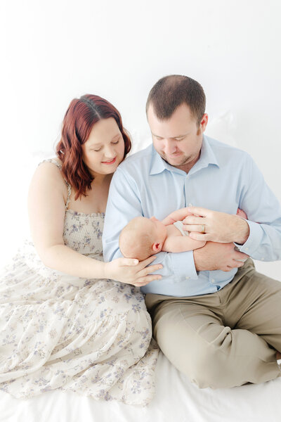 A mom and dad sitting on a bed holding and looking at their newborn baby at a photography studio in Panama City, FL.