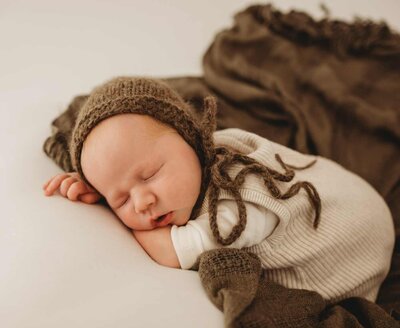 Ruua Hamdan Photography (Altrincham/Manchester, UK): A sleeping baby wearing a brown bonnet.