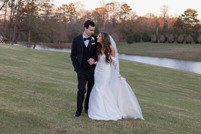Bride and groom walk through a field at sunset