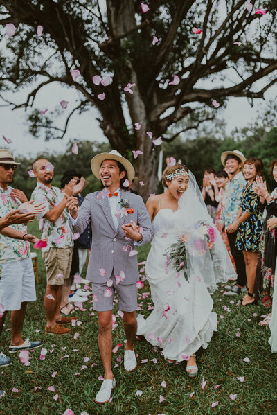 Stylish Japanese wedding couple walks back down the aisle after their wedding ceremony at Sunset Ranch while their guests throw flower petals during the recession.
